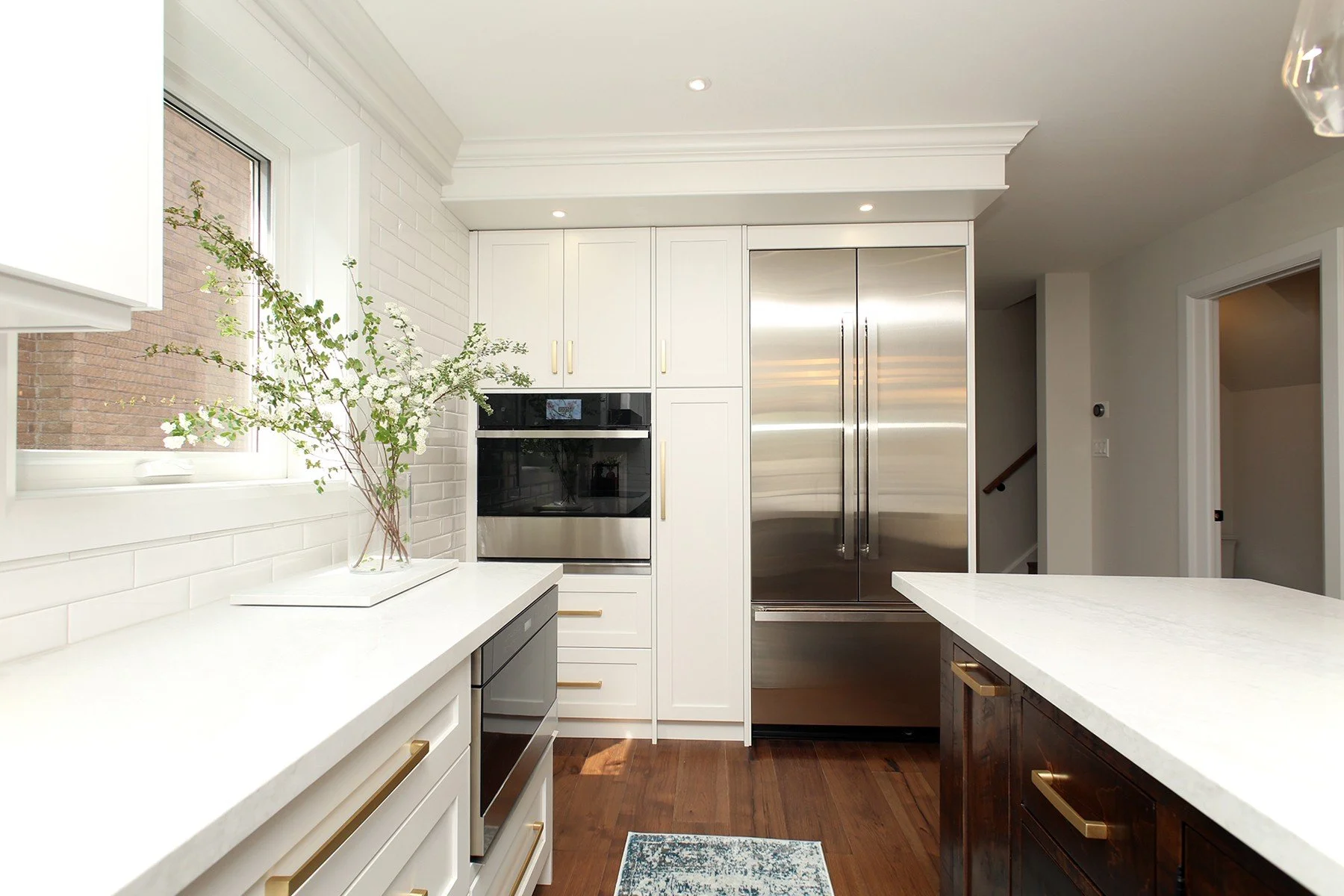 Contemporary Toronto kitchen with warm white cabinets, quartz countertops, a dark wood island, and brushed brass hardware.