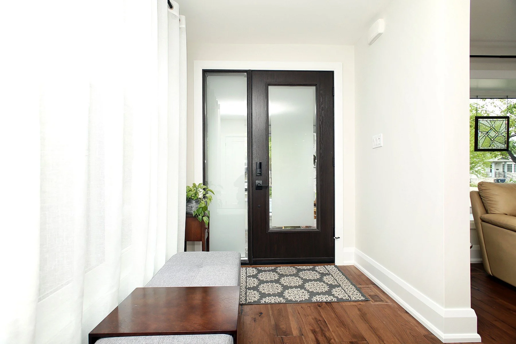 A clean entry features a frosted glass double door, patterned rug, and wood bench.
