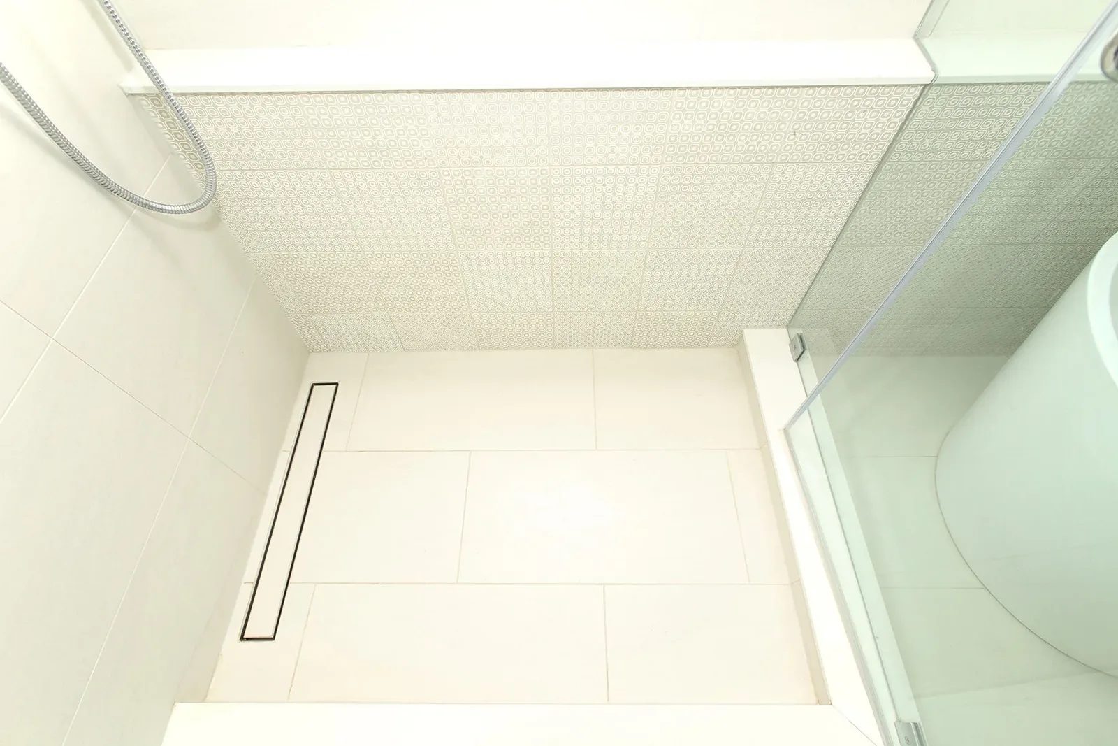 Warm white shower detail with large wall tiles, a linear drain, glass partition, and chrome fixtures.
