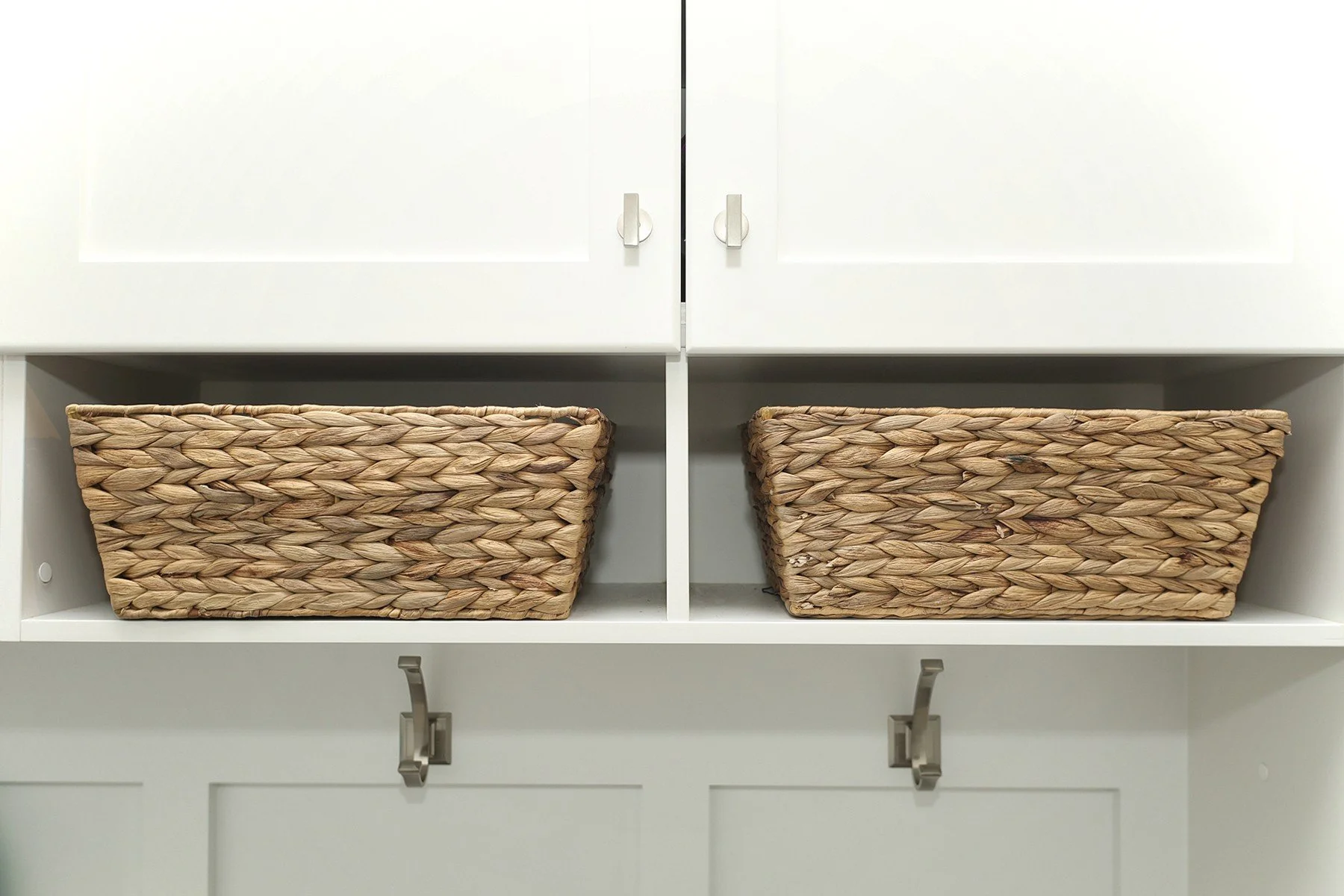 White built-in entry storage with woven baskets, upper cabinets, and brushed metal hooks.