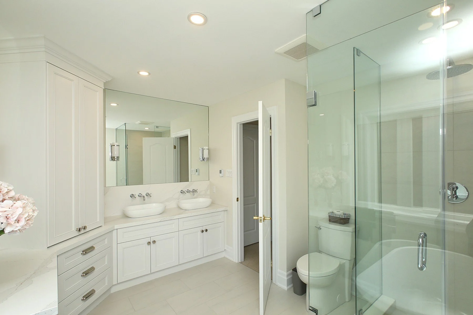 Bright finished bathroom with double vanity, vessel sinks, and a glass enclosed tub and shower.
