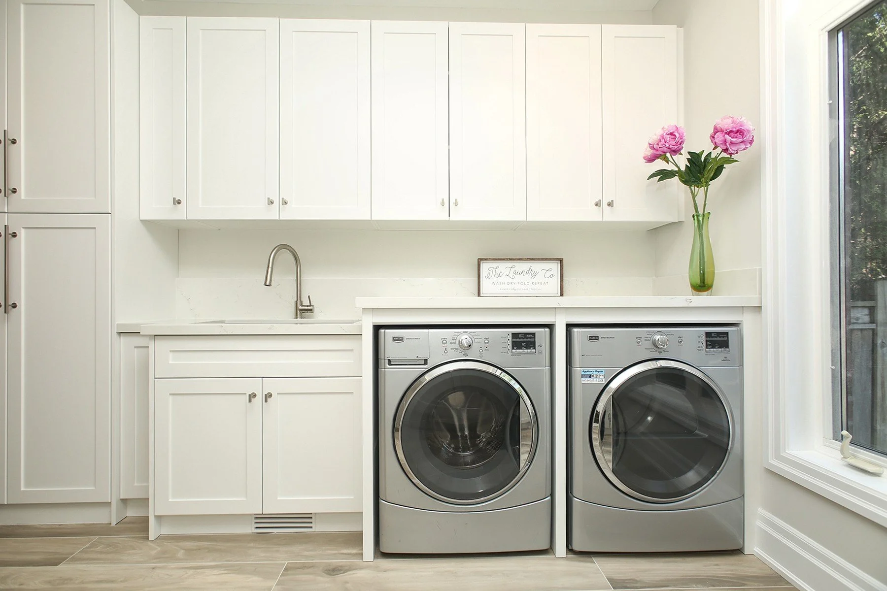 Bright laundry room with white shaker cabinets, a sink, and side by side front load machines.