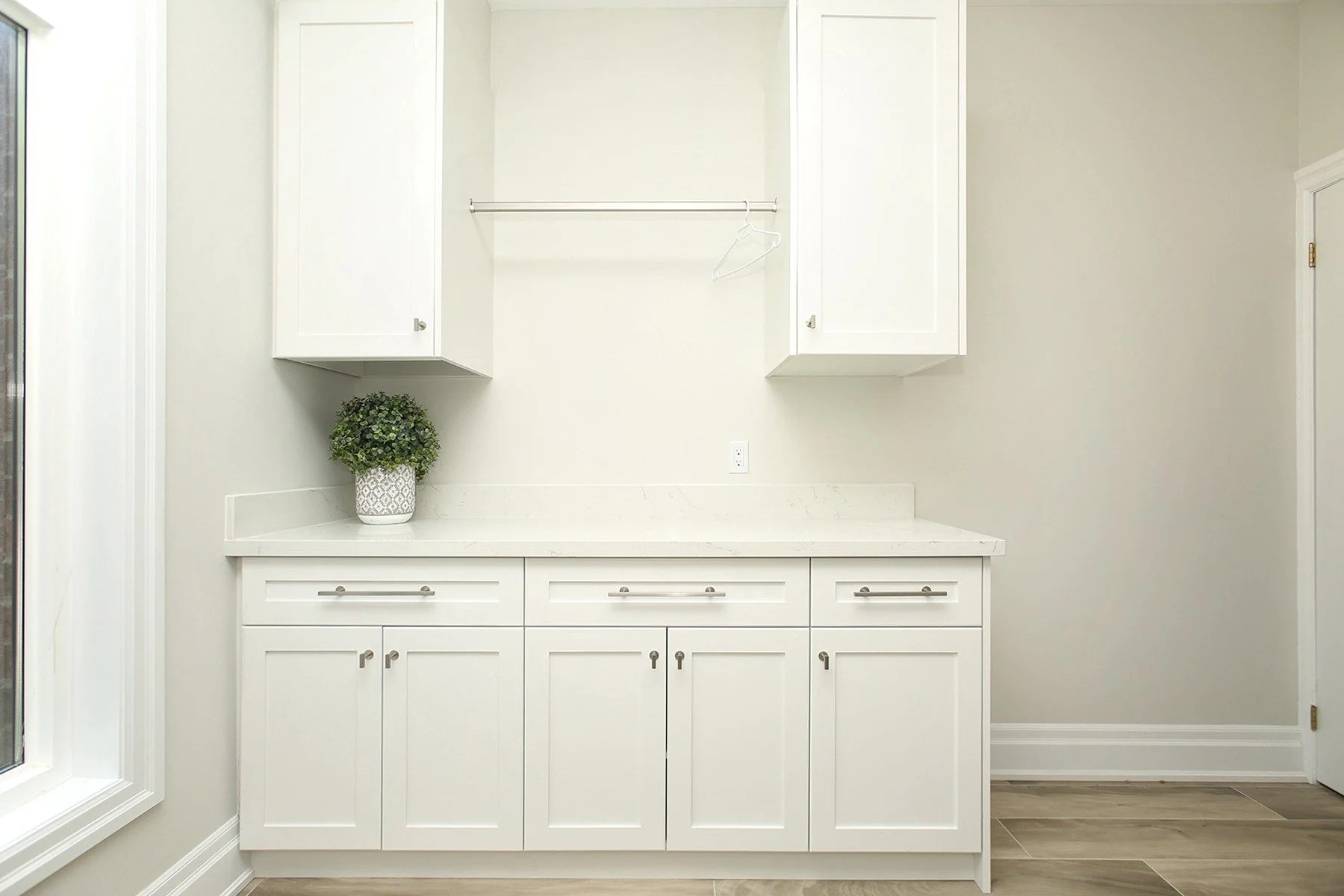 Bright laundry room with white shaker cabinets, quartz counter, hanging rod, and light grey walls.