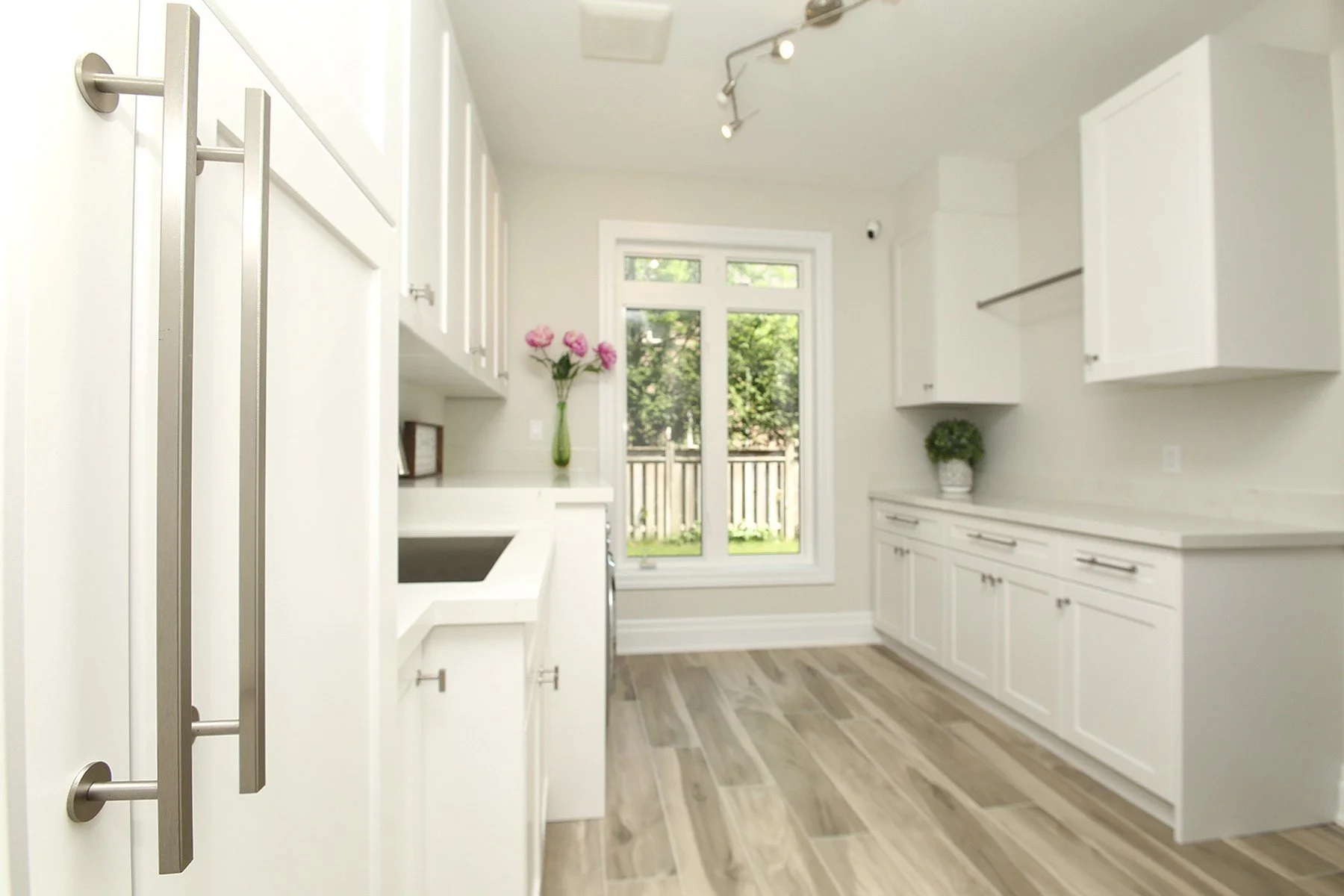 Bright white laundry room with shaker cabinets, quartz counters, a sink, and a large rear window.
