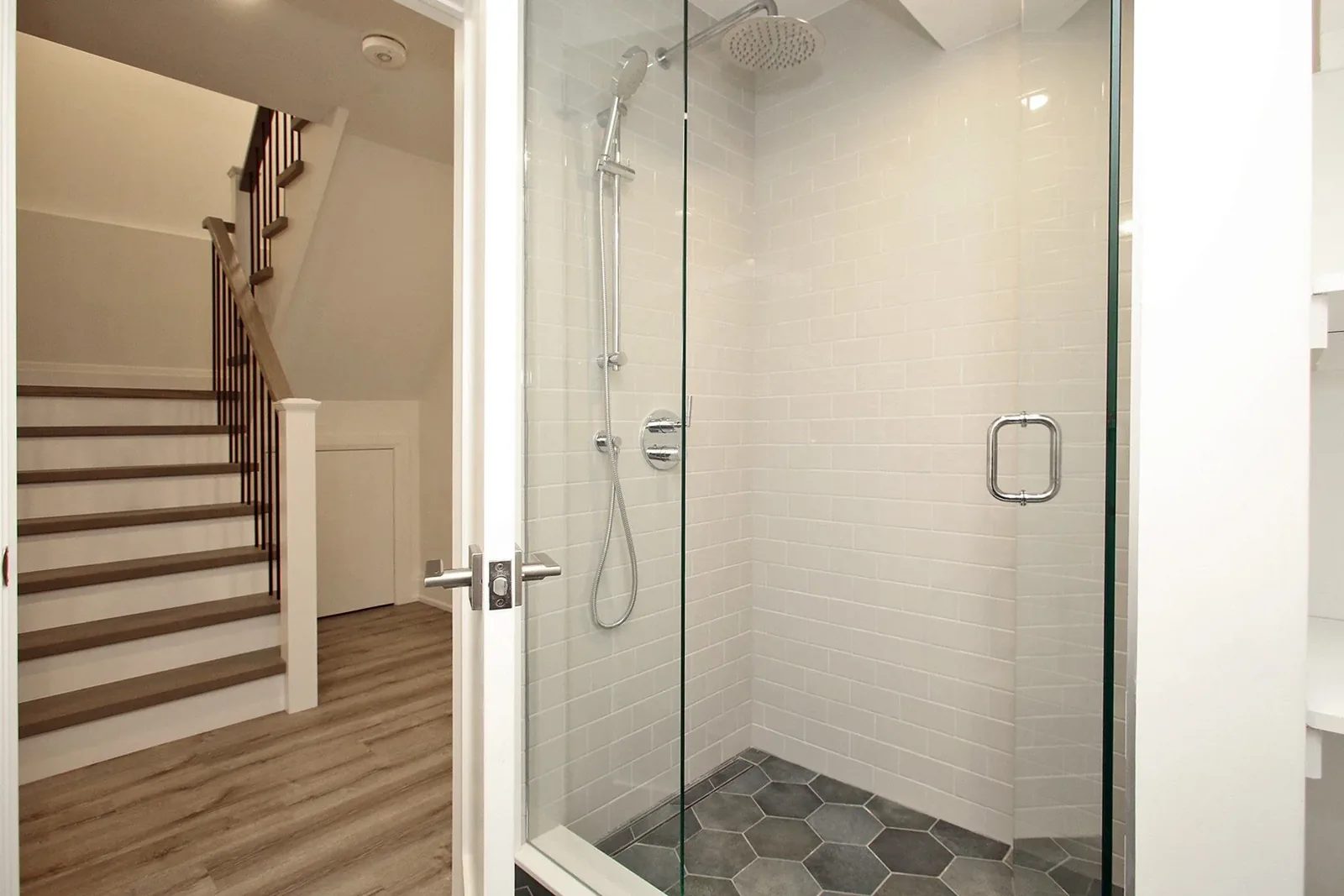 Glass-enclosed walk-in shower with white subway tile, charcoal hex floor, and rainfall chrome head.