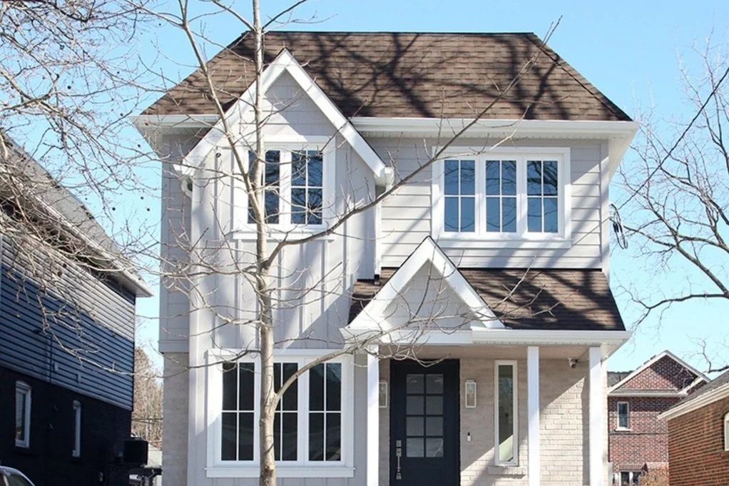 Front elevation of a newly built two-storey white infill home with covered porch on a snowy winter street.