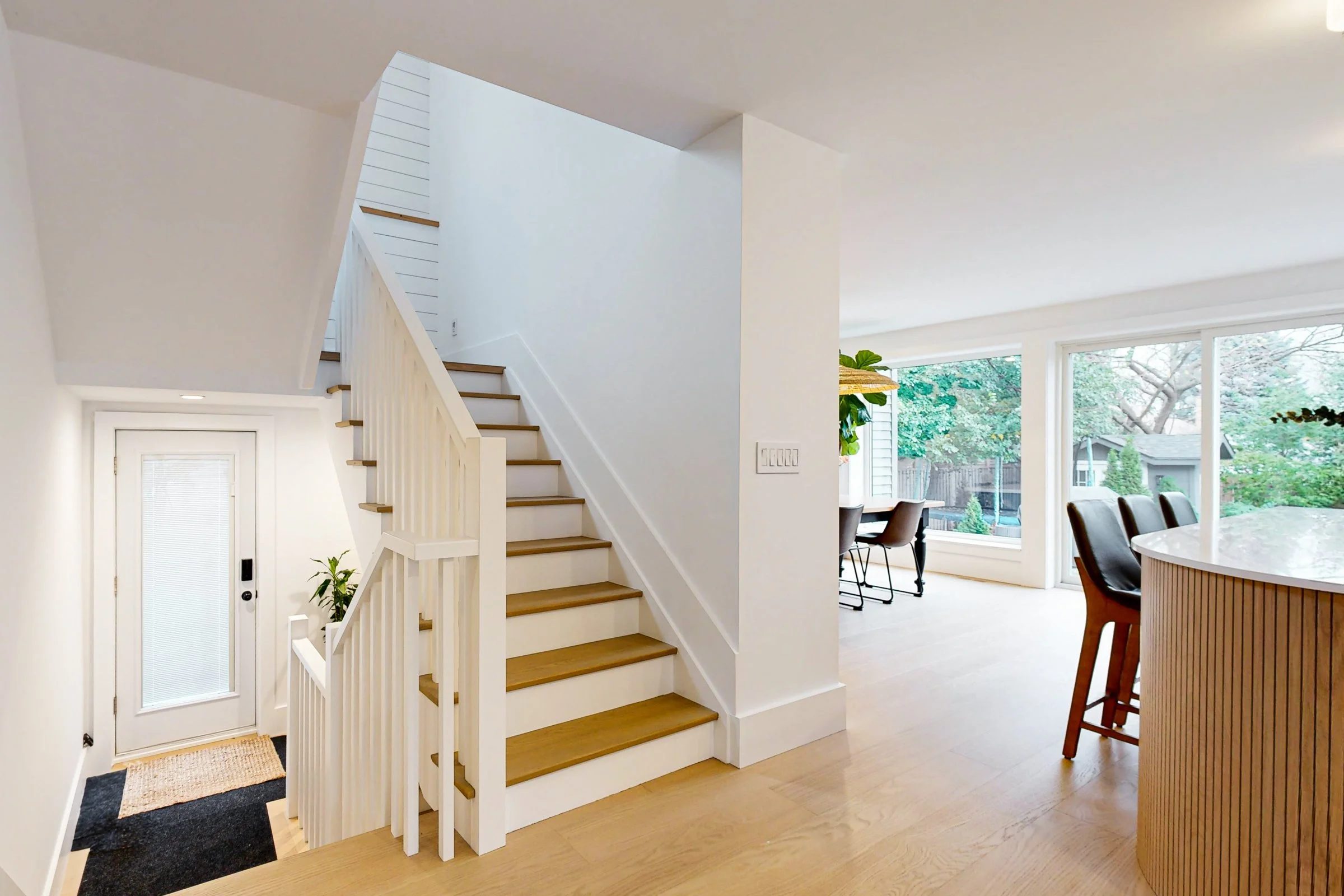 Bright open entry with oak stairs, white millwork, and large rear windows beside the dining area.