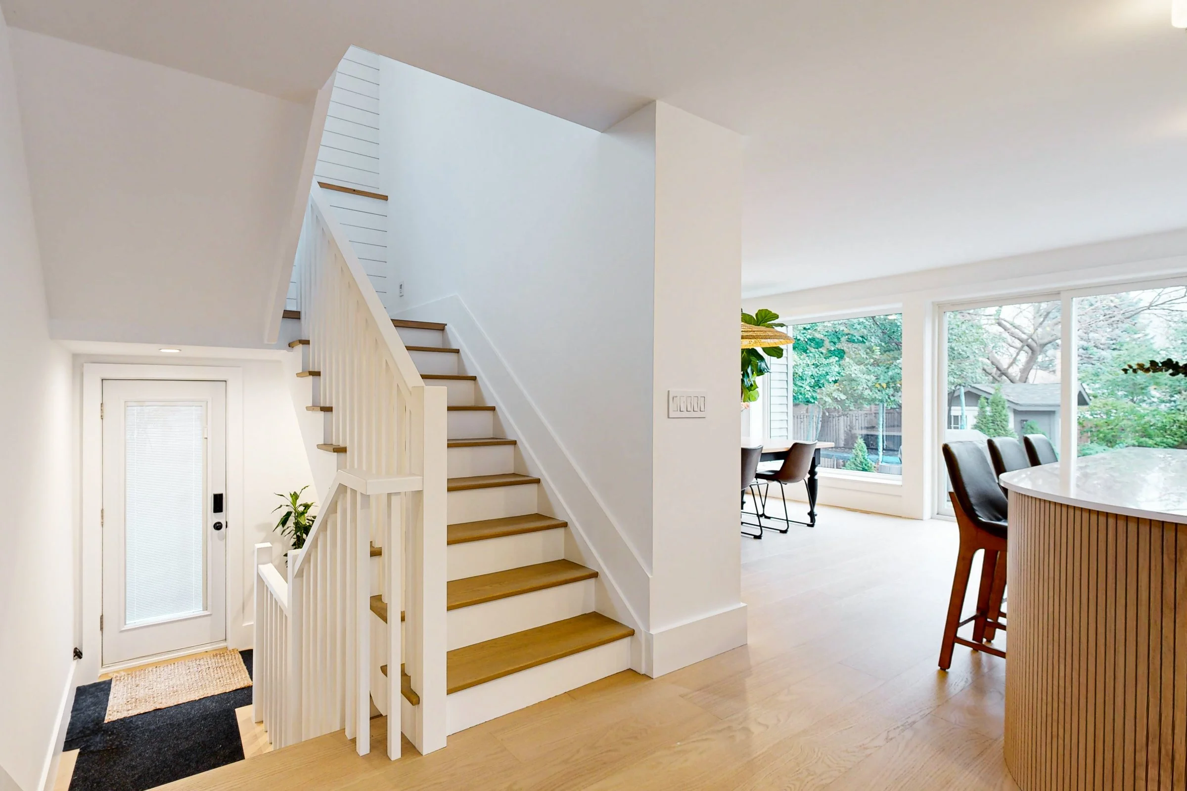 Bright open entry with oak stairs, white millwork, and large rear windows beside the dining area.