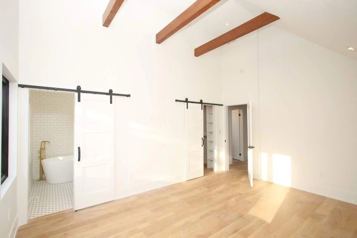 Primary bedroom with a vaulted wood-beam ceiling and a sliding barn door opening to an ensuite with a freestanding tub.