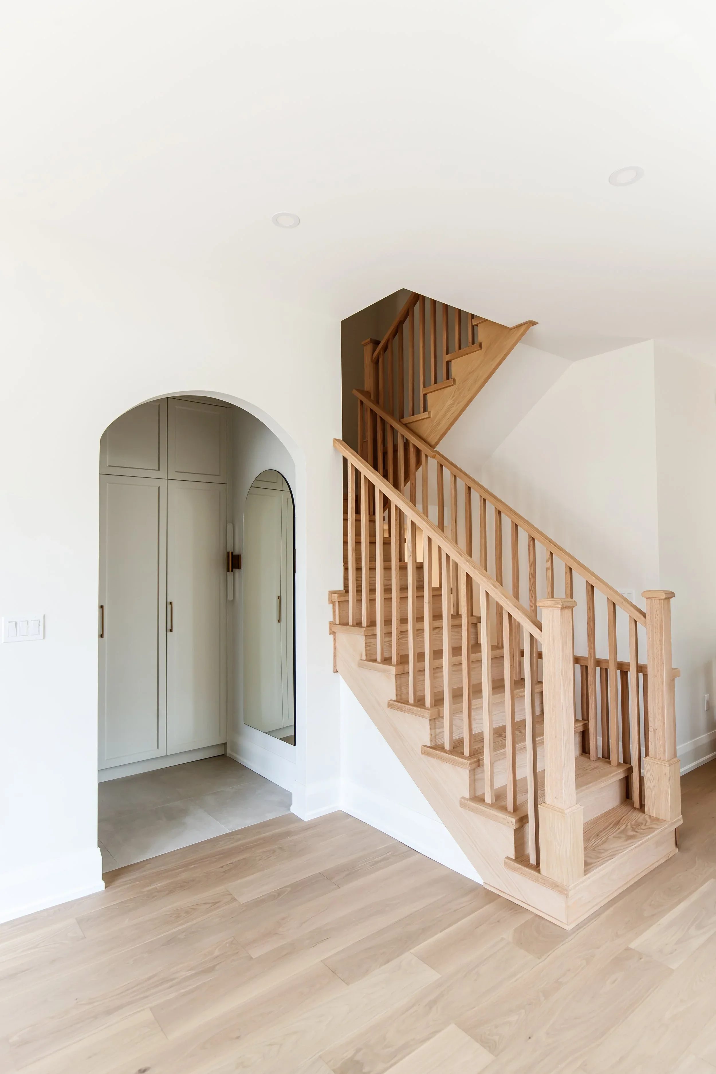 White oak open-tread staircase beside an arched entry to a built-in mudroom.