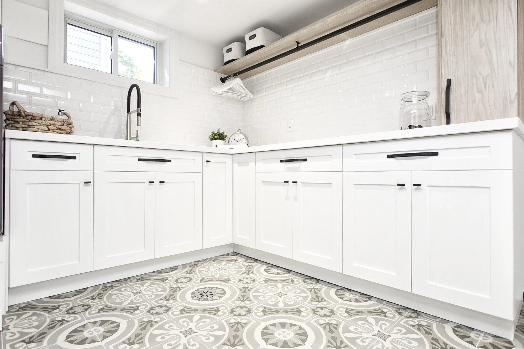 Bright white laundry room with shaker cabinets, black hardware, subway tile, and side-by-side machines.