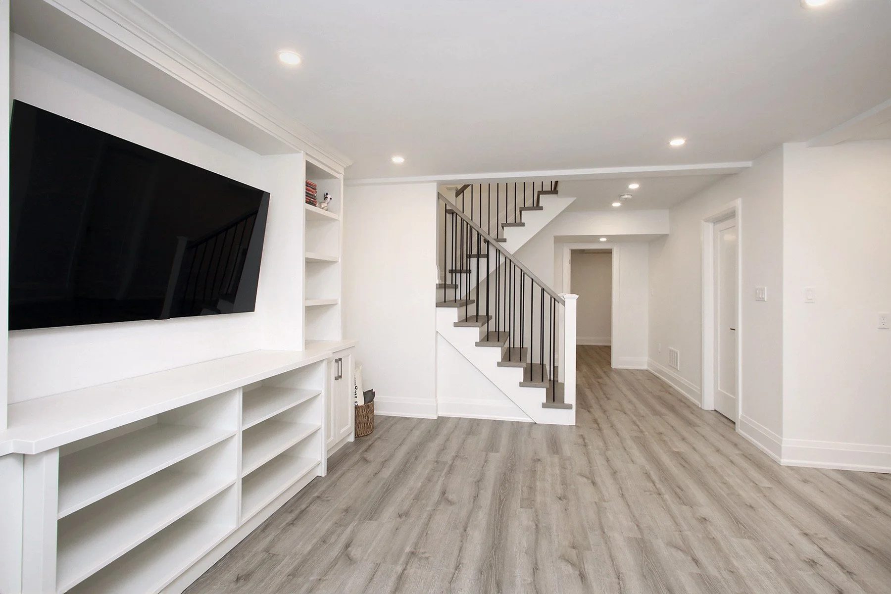 Finished basement recreation room with white built-in media unit and mounted television.