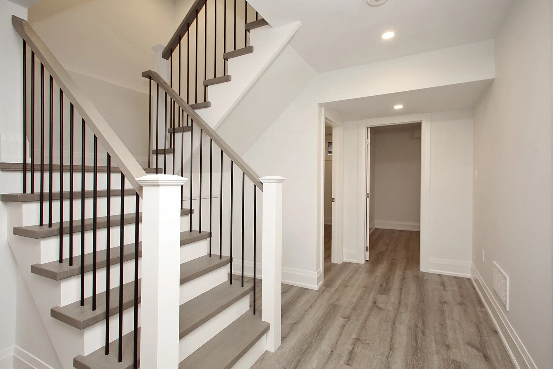 Basement landing with open staircase, black metal spindles, and grey vinyl plank flooring.