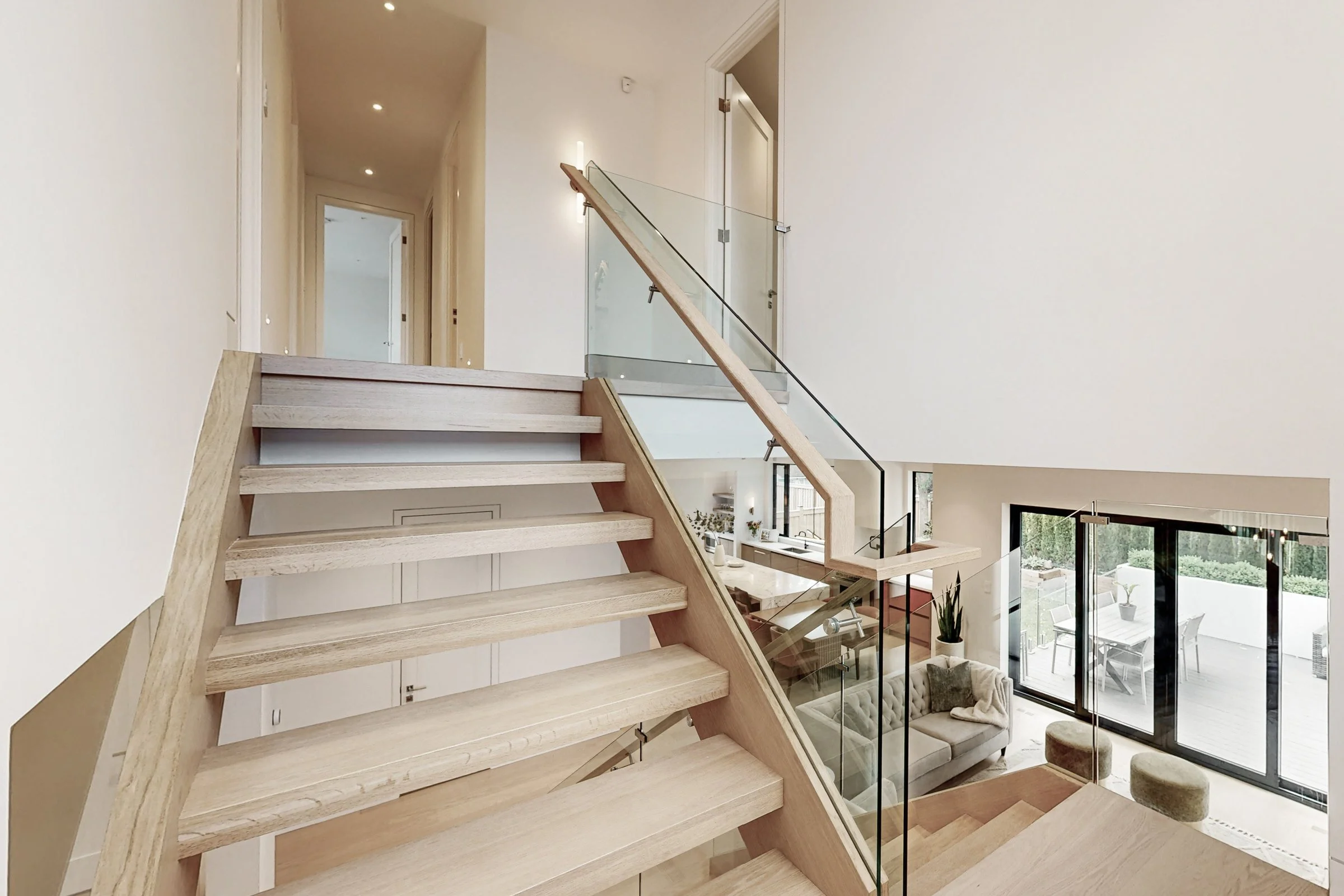 Mid-landing view down the open oak staircase with glass railings overlooking the main floor.