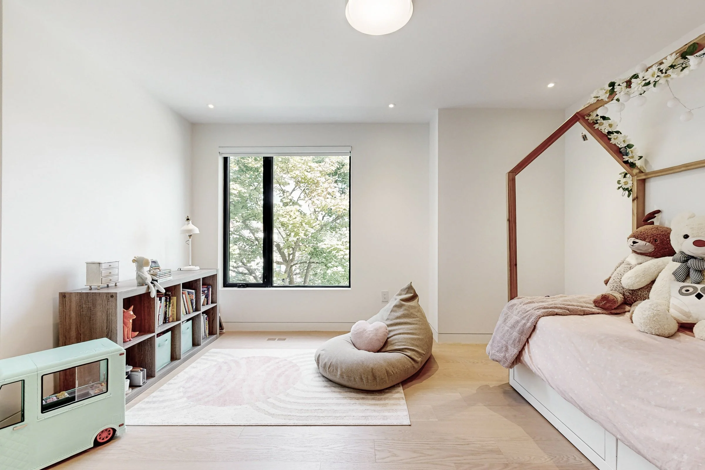 Child bedroom with white house-frame bed, pink bedding, bookcase cubbies, and bench seat.