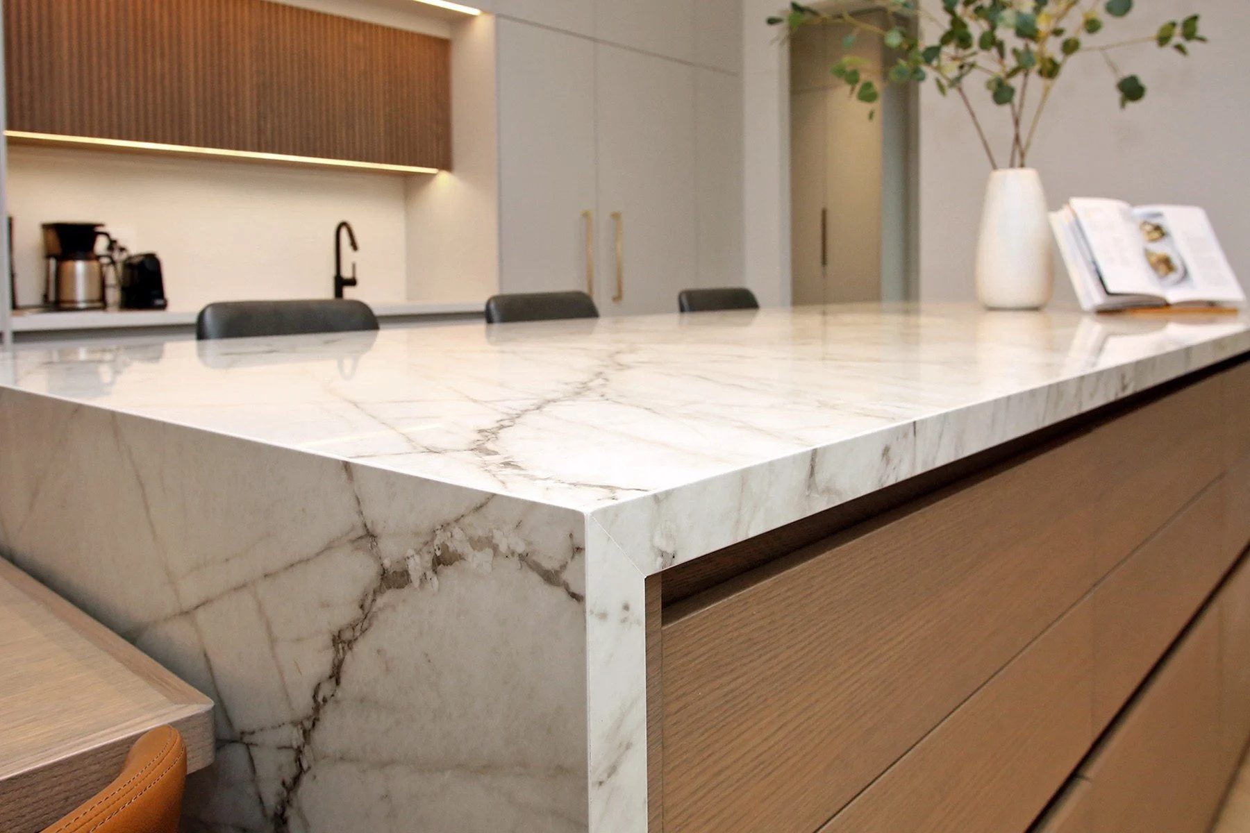 Mitred calacatta marble waterfall detail meets rift-sawn oak island drawers under warm ambient lighting.