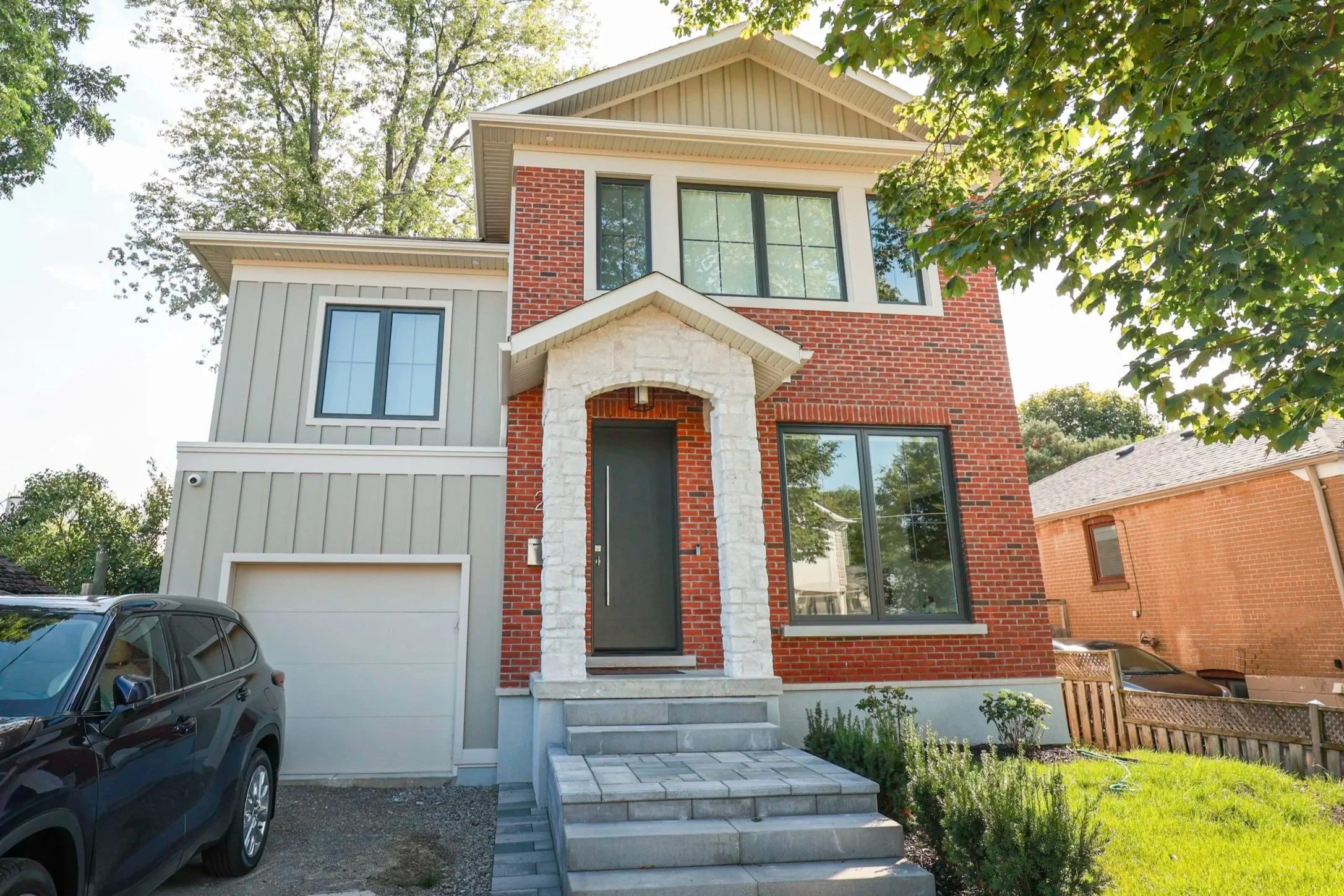 Front elevation of a completed two-storey Toronto home with brick and board-and-batten cladding and a stone entry portico.