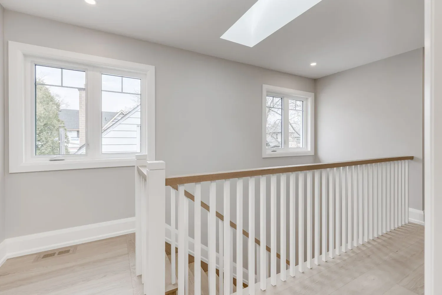 After renovation by Waterfront, an upper landing with skylight, white balustrade, and natural wood handrail in Etobicoke.
