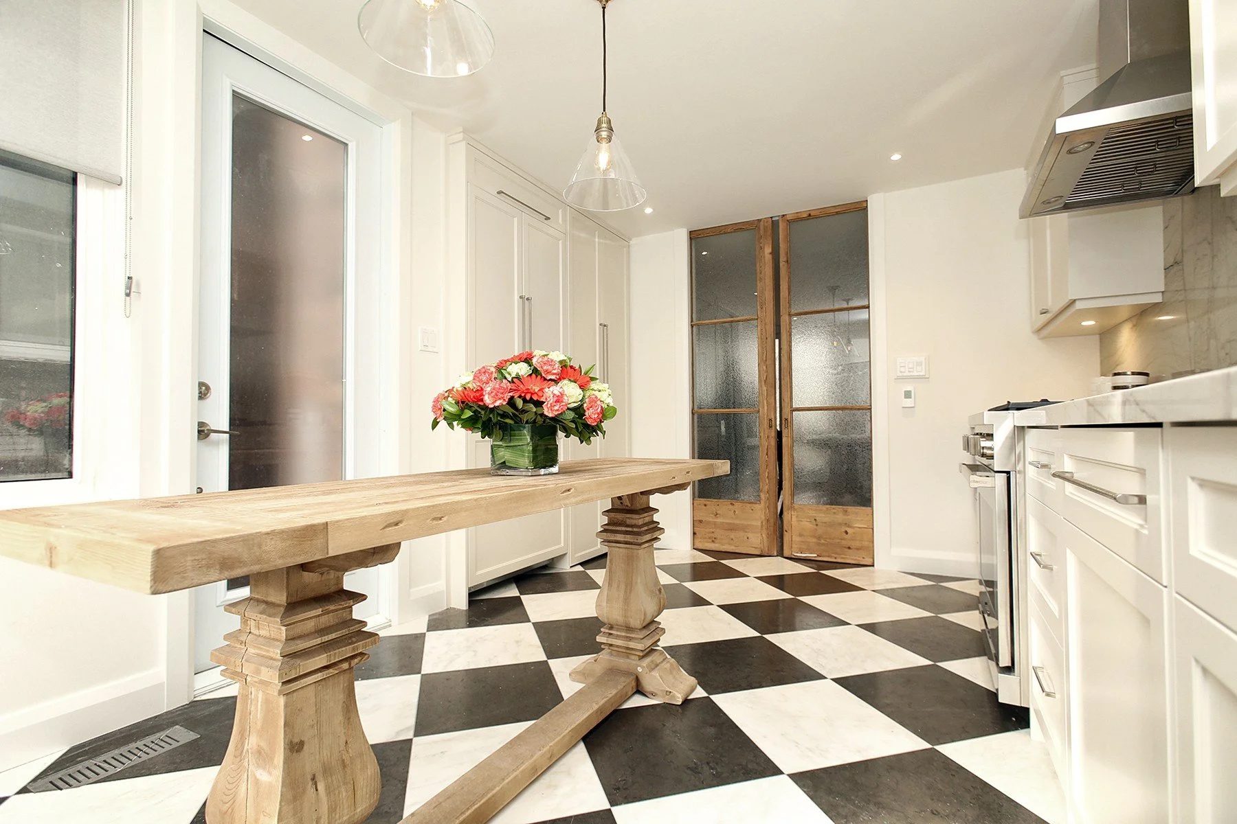 Bright renovated kitchen with white shaker cabinets, checkerboard tile, and a rustic oak table.
