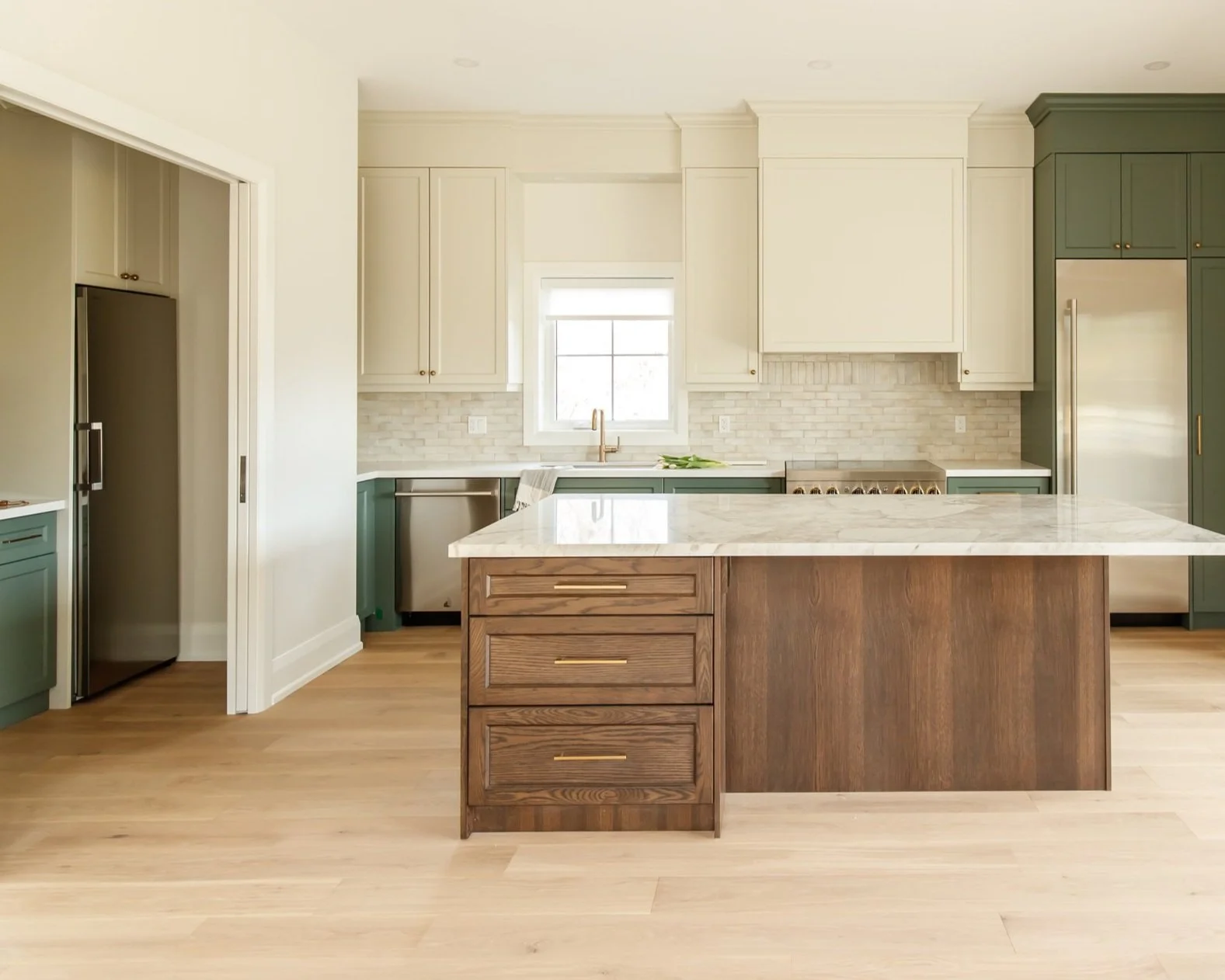 Open plan kitchen view with a wide stained oak island facing a glass stair screen.