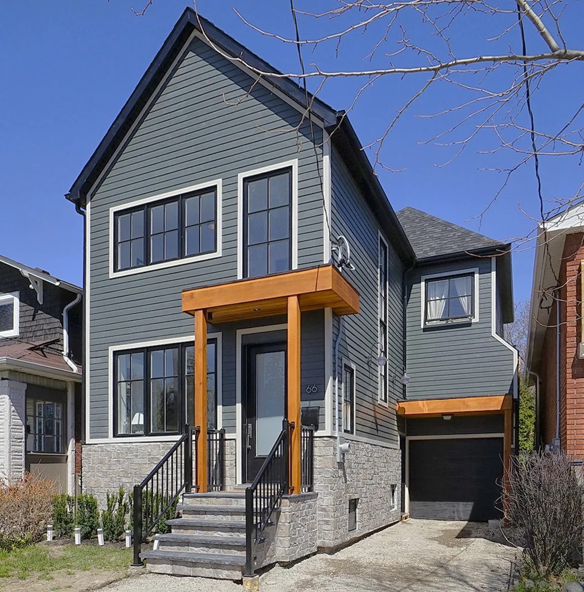 Completed second storey addition with grey horizontal siding, black-trimmed windows, cedar porch posts, and a stone base.