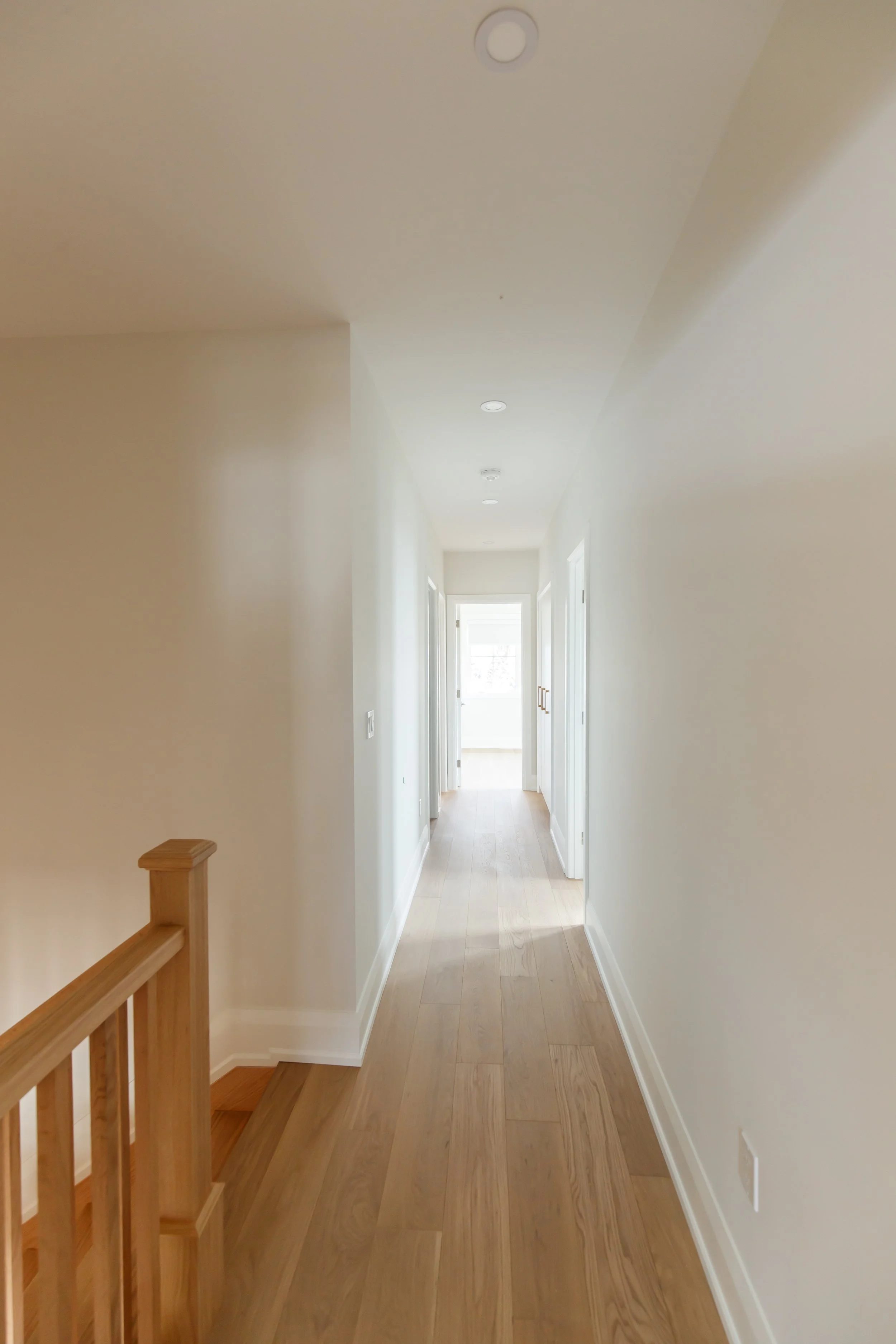 Long bright upper hallway with recessed ceiling lights and light oak flooring.
